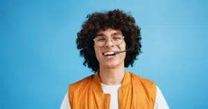 Lachende jongeman met headset en bril voor een blauwe achtergrond tijdens training strategisch salesgesprek voeren