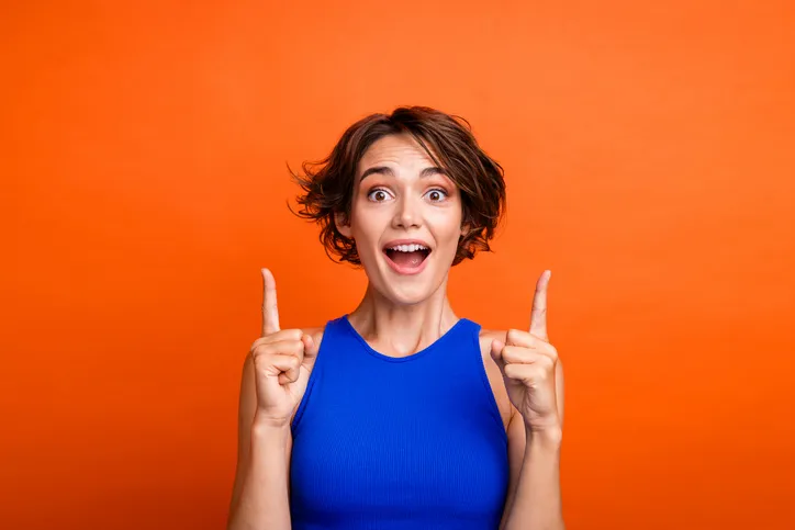 Jonge, lachende vrouw die omhoog wijst als symbool voor positiviteit over AI-Geletterdheid