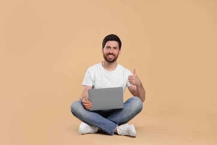 Positieve man met laptop op schoot en duim omhoog als symbool voor goede samenwerking
