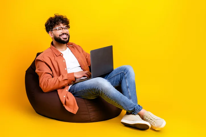 Lachende man met laptop op schoot als symbool voor ontwikkeling en investeren in jezelf deze zomer