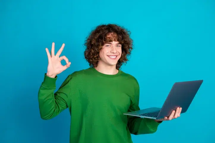 Jonge man met laptop die het 'oké' signaal maakt als teken van bij zijn op het gebied van AI-geletterdheid